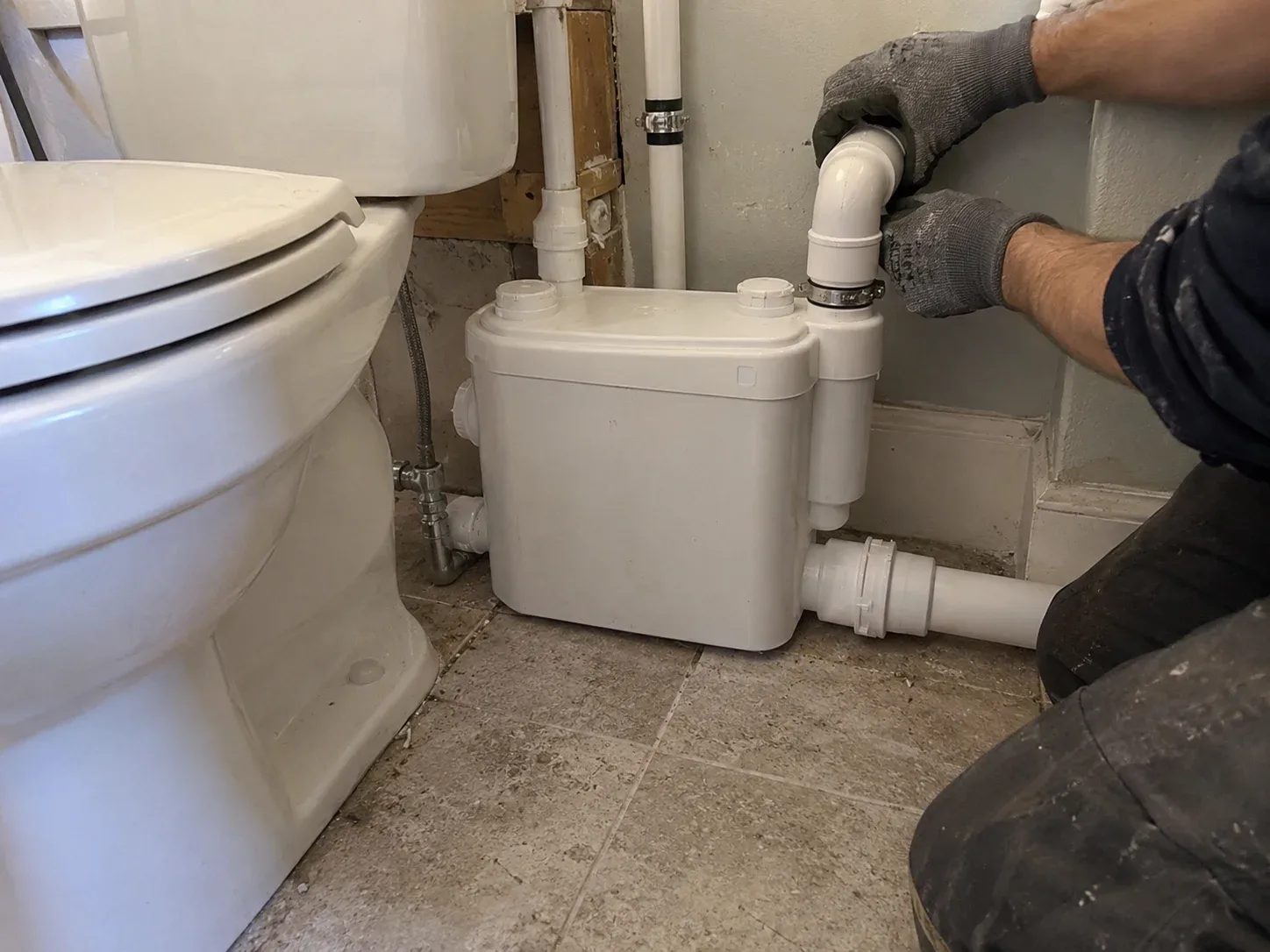 Technician connecting a compact macerating grinder pump behind a basement toilet in Kitchener