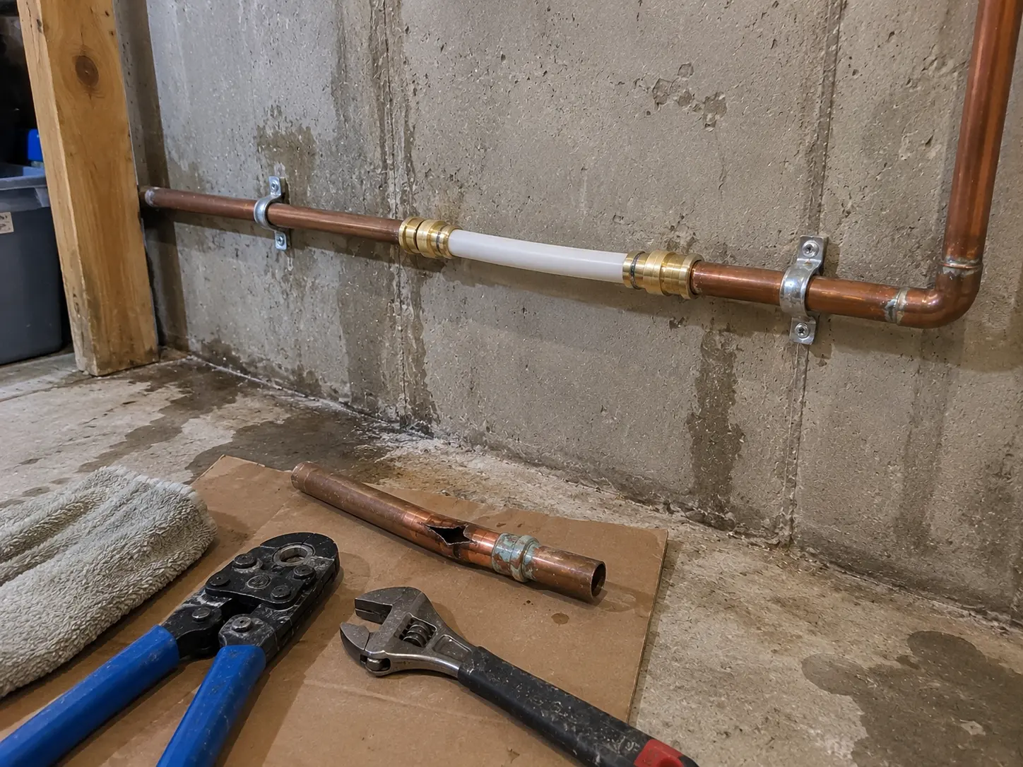 Repaired copper water pipe with brass fittings and plumbing tools in a Kitchener basement